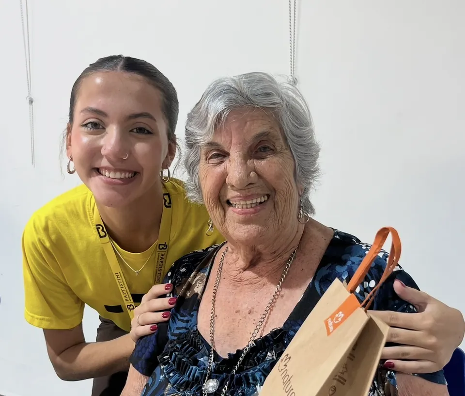 Integrante da equipe abraçada a uma moradora do Lar dos Velhinhos, que segura um presente